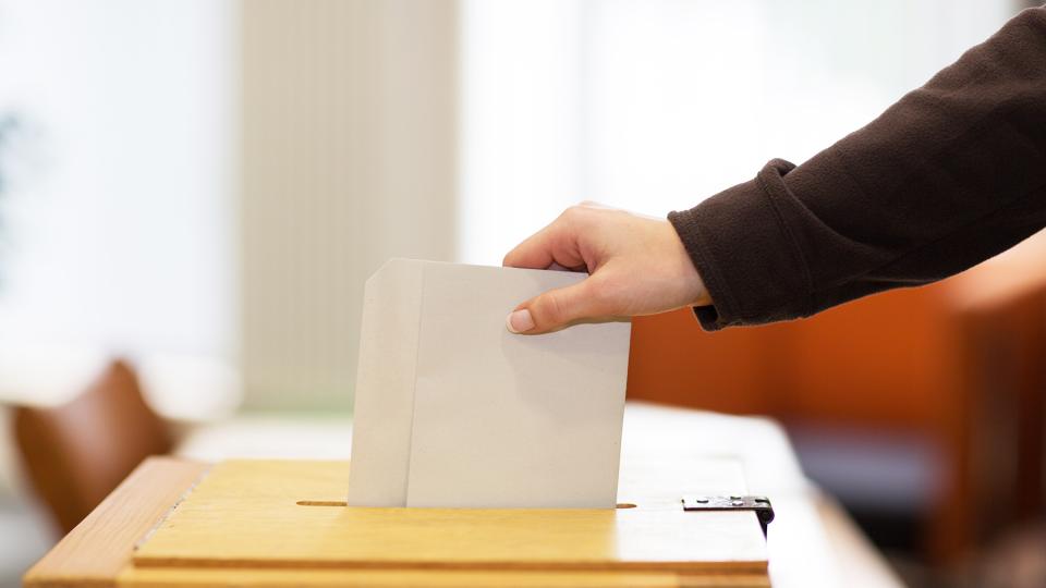 Wahlzettel wird in eine Wahlurne gesteckt