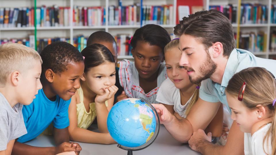 Grundschulklasse sitzt mit einem Lehrer um einen Globus