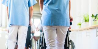 Altenpfleger schieben Senioren im Rollstuhl durch Altenheim